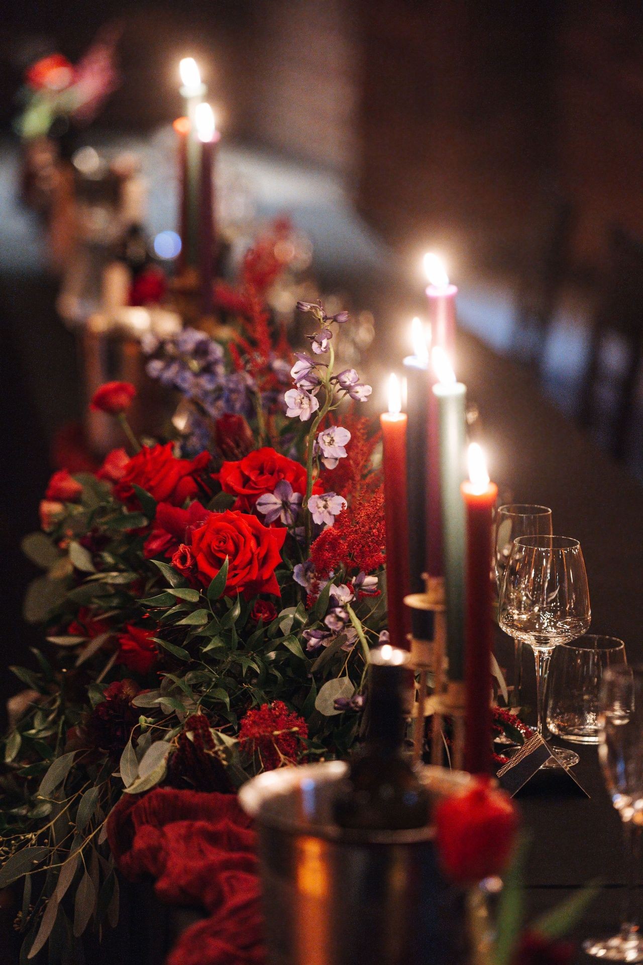 Elegant table setting with red roses, purple flowers, lit candles, and wine glasses.