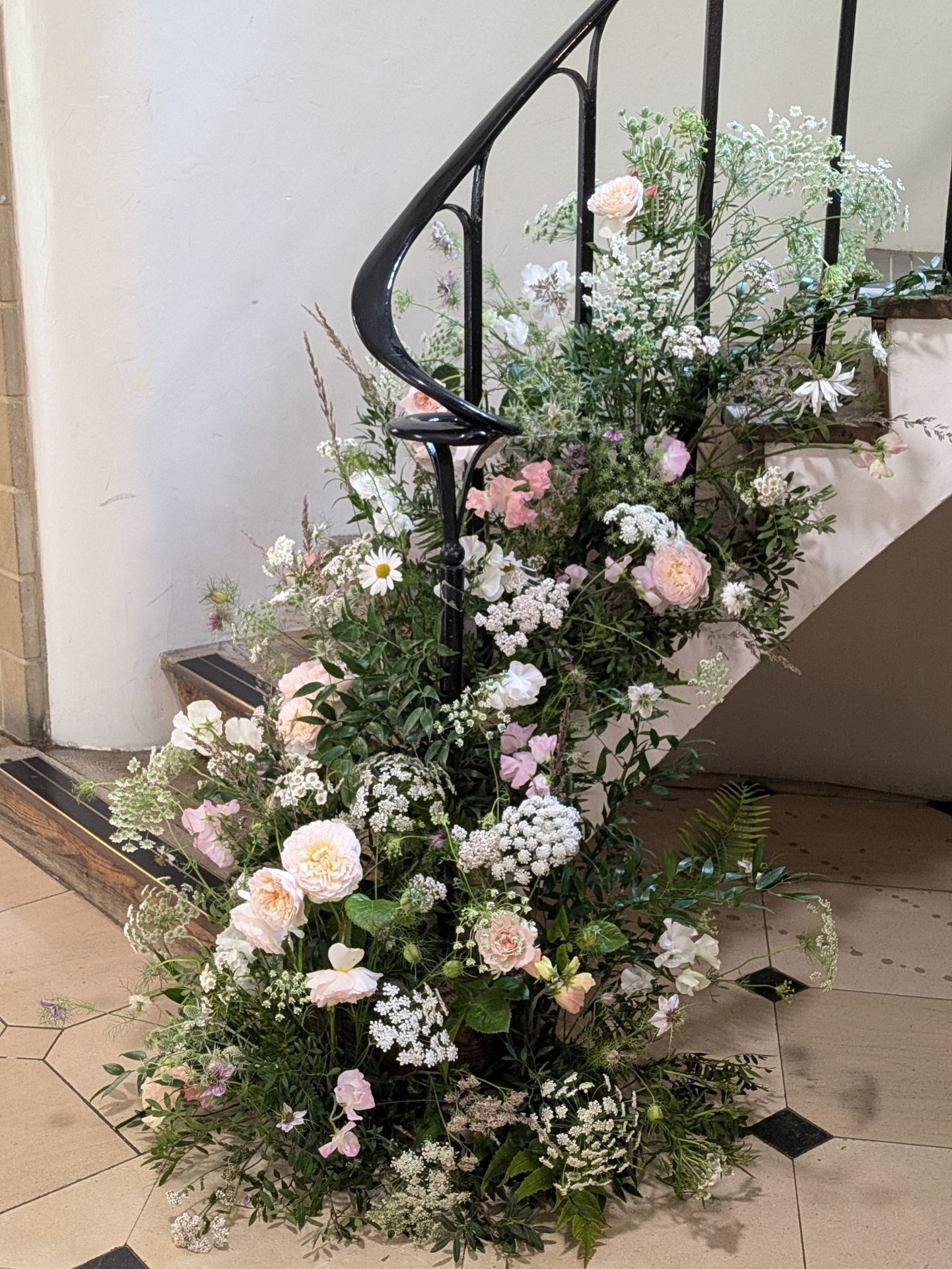 Elegant staircase adorned with lush floral arrangements featuring white and pink flowers and green foliage.