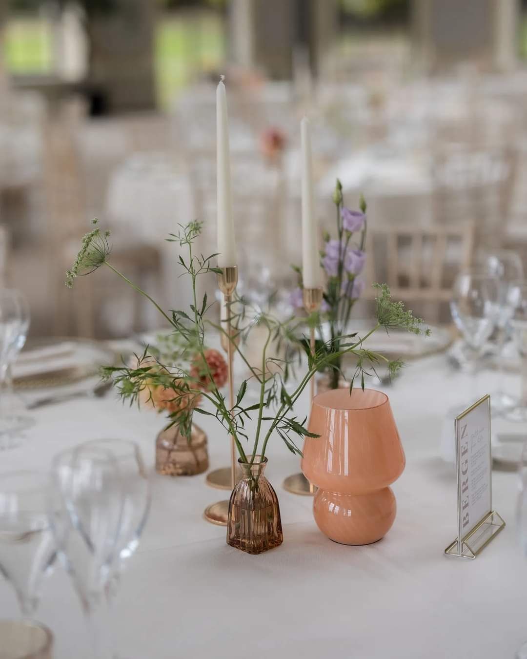 Elegant table setting with flowers, taper candles, and a peach vase on a white tablecloth.